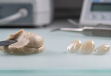 A close-up, photorealistic image displaying two types of dental veneer materials side-by-side on a clean, modern surface. On the left is a sculpted piece of tooth-colored composite resin, and on the right are several finished, translucent porcelain veneers.