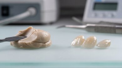 A close-up, photorealistic image displaying two types of dental veneer materials side-by-side on a clean, modern surface. On the left is a sculpted piece of tooth-colored composite resin, and on the right are several finished, translucent porcelain veneers.