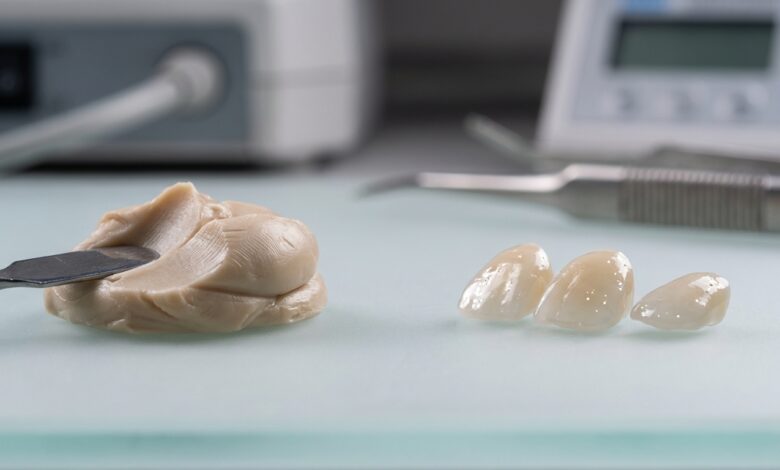 A close-up, photorealistic image displaying two types of dental veneer materials side-by-side on a clean, modern surface. On the left is a sculpted piece of tooth-colored composite resin, and on the right are several finished, translucent porcelain veneers.