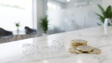 A photorealistic close-up of a clear Invisalign aligner next to a stack of blurred British Pound coins on a white marble surface, symbolizing the cost of orthodontic treatment in the UK.