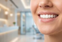 A detailed close-up photograph of a person's healthy, bright white teeth and radiant smile. The background is a softly blurred, modern dental office, emphasizing a professional and clean environment.