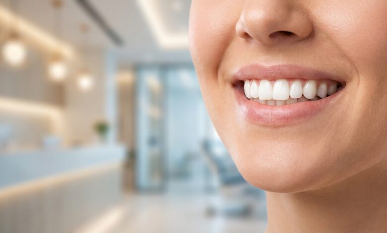 A detailed close-up photograph of a person's healthy, bright white teeth and radiant smile. The background is a softly blurred, modern dental office, emphasizing a professional and clean environment.