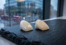 A photorealistic close-up of a high-quality porcelain veneer and a composite veneer on a clean surface, with a blurred background of a modern UK city, symbolizing the cost of cosmetic dentistry.