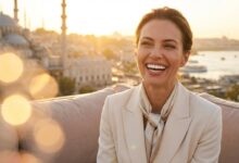 A confident woman with a beautiful, flawless white smile stands on a balcony with a blurred Turkish city skyline behind her at sunset.
