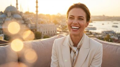 A confident woman with a beautiful, flawless white smile stands on a balcony with a blurred Turkish city skyline behind her at sunset.
