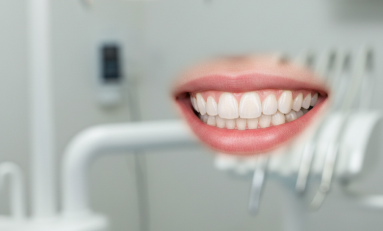 A close-up, photorealistic image of a perfect, radiant smile with healthy, bright, and perfectly aligned teeth. The background is a softly blurred, clean, and modern dental clinic interior.