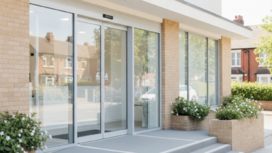 A modern, clean dental clinic building entrance with light-colored walls, large windows, and an inviting doorway, bathed in natural daylight. The background is softly blurred, hinting at a typical British street or residential area. There is no visible text, logos, or branding.
