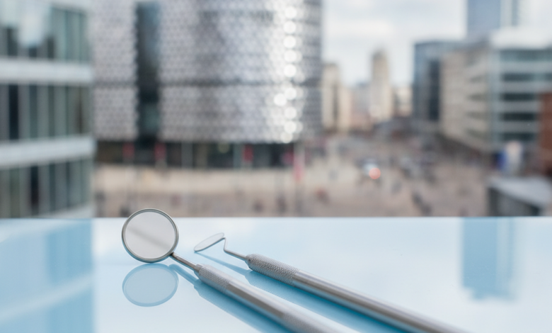 Close-up of modern, sterile dental instruments on a tray, with a softly blurred cityscape of Birmingham, UK, in the background. The image signifies professional dental services and urban healthcare.