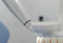 A close-up, photorealistic image of a sophisticated dental laser emitting a focused beam of light onto a tooth or gum, set against a blurred background of a modern dental clinic.
